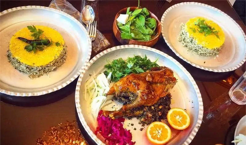 تصویری از میز غذا در رستوران خوان باشی با مرغ شکم پر مجلسی، دو پرس سبزی پلو زعفرانی و سالاد تازه. تجربه غذای اصیل ایرانی.