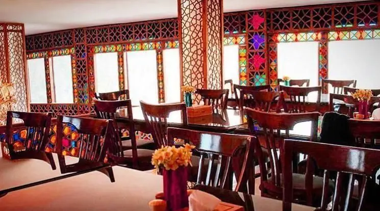 فضای داخلی رستوران خوان باشی با پنجره‌های ارسی سنتی ایرانی، شیشه‌های رنگی و میز و صندلی‌های چوبی شیک.