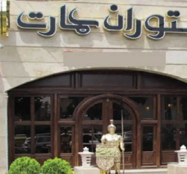 نمای بیرونی رستوران ایرانی عمارت با ورودی چوبی شیک، تابلوی زیبا و مجسمه سرباز باستانی در مقابل ورودی، مکانی دلنشین برای غذای ایرانی.