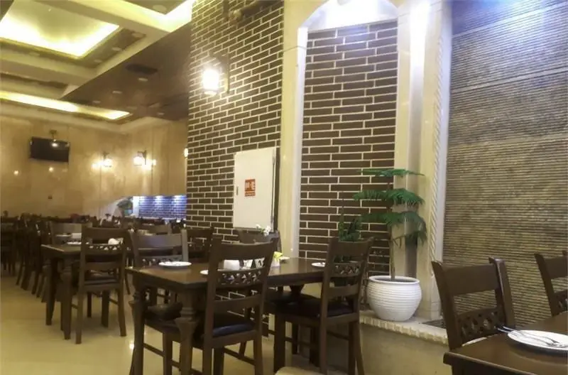 فضای داخلی دنج و شیک رستوران ایرانی عمارت با میز و صندلی‌های چوبی، دکوراسیون آجری و نورپردازی گرم، آماده میزبانی از مهمانان.