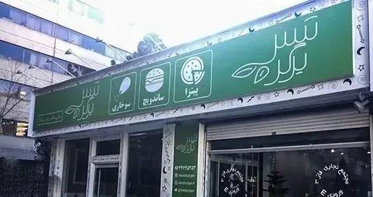 نمای بیرونی فست فود تیس برگر با تابلوی سبز رنگ که لوگوی تیس برگر و خدمات ساندویچ، پیتزا و سوخاری را معرفی می‌کند.