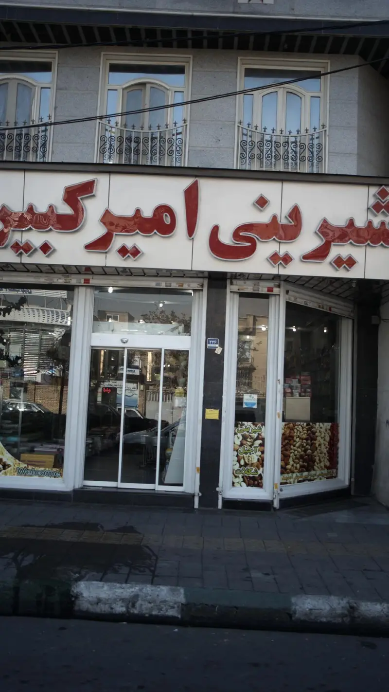 تصویری از نمای بیرونی شیرینی و قنادی امیرکبیر، فروشگاهی با ویترین‌های پر از آجیل تازه، خشکبار و انواع شیرینی.