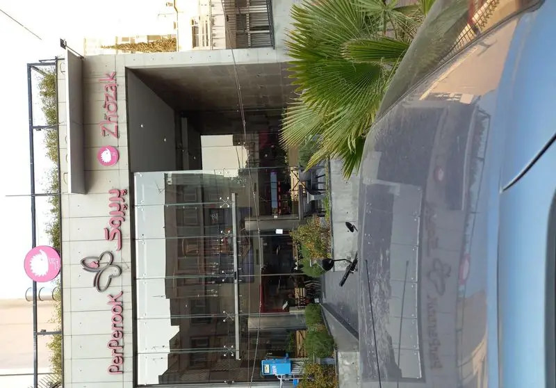 نمای خارجی ساختمان رستوران و فست فود پرپروک به همراه تابلوی ژوژک. ورودی شیشه‌ای مدرن و فضای سبز شهری در جلوی شعبه.