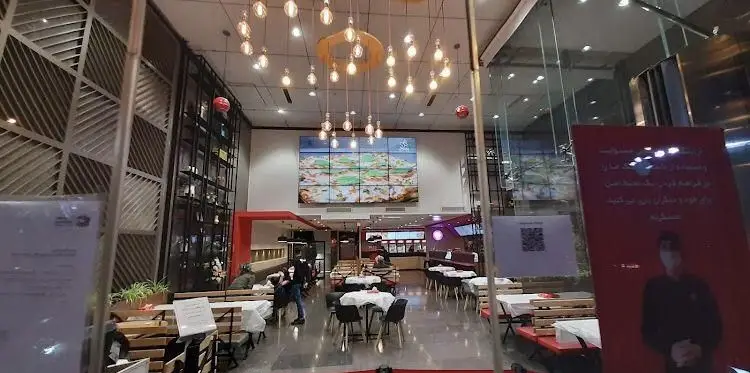 نمای داخلی رستوران پرپروک با طراحی مدرن، میز و صندلی‌های چیده شده، صفحه نمایش بزرگ پیتزا و نورپردازی جذاب. محیطی دلنشین برای مشتریان.