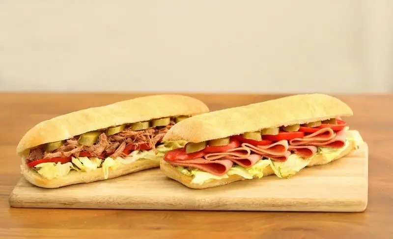 دو ساندویچ پرپروک با نان باگت بلند و تازه، یکی با گوشت ریش ریش و دیگری با ژامبون، هر دو با کاهو، گوجه، سس و خیارشور. غذای آماده عالی پرپروک.