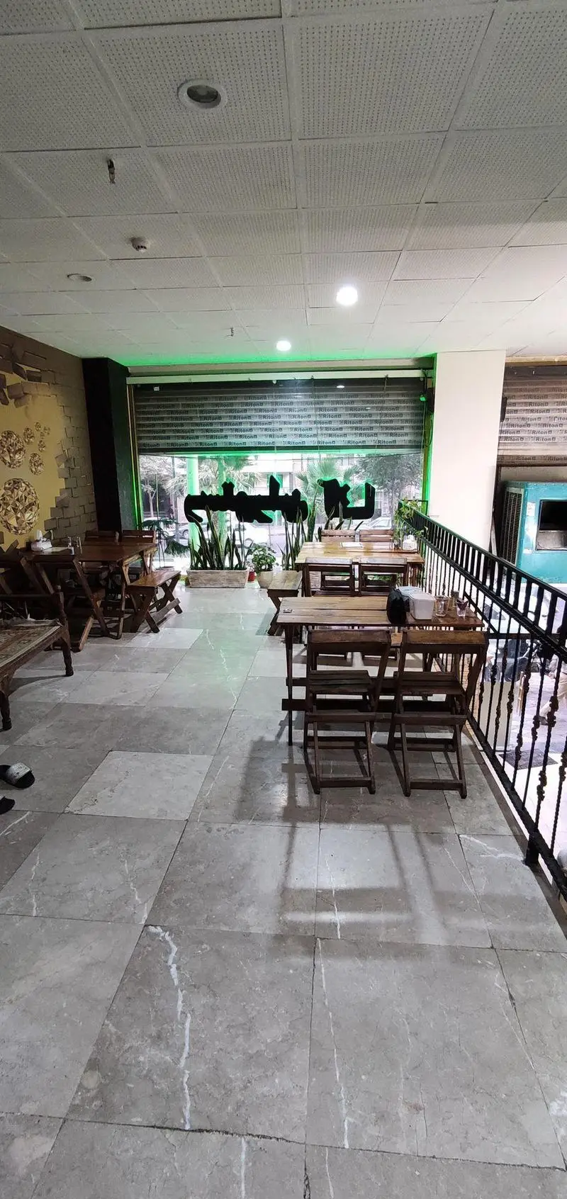 محیط دنج و زیبای رستوران غذا خونگی انا با میز و صندلی‌های چوبی، دکوراسیون خاص و نورپردازی سبز برای سرو غذاهای خانگی.