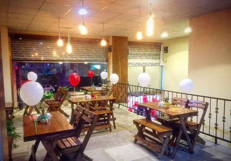 فضای داخلی رستوران غذا خونگی انا با میز و صندلی چوبی، دکوراسیون بادکنکی قرمز و سفید و نورپردازی دلنشین برای مشتریان.