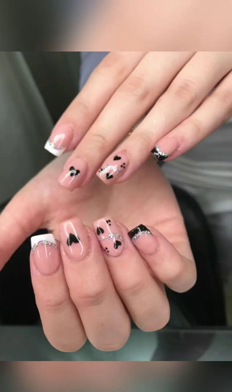 طراحی ناخن فانتزی و دخترانه با لاک ژل صورتی ملایم، فرنچ سفید و مشکی، طرح قلبهای کوچک و خطوط اکلیلی نقرهای شیک