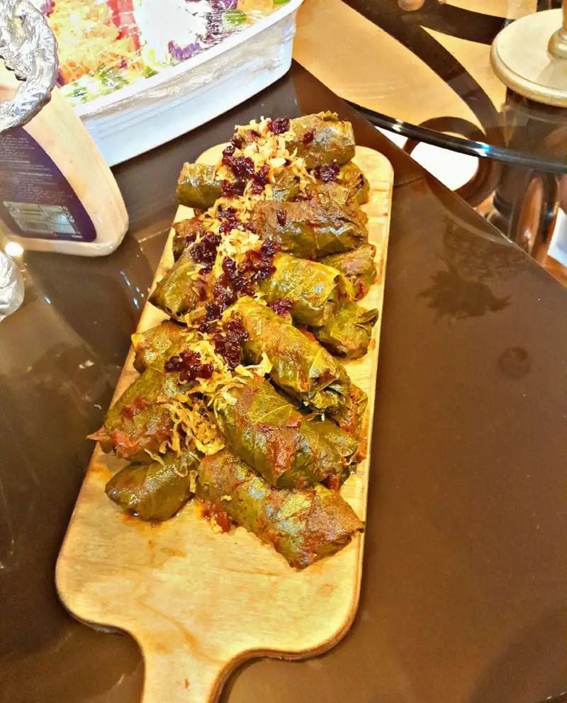 دلمه برگ موی مجلسی، غذای سنتی ایرانی از کترینگ و تشریفات Lemon. در سینی چوبی با زرشک و پیاز داغ برای پذیرایی مهمانی‌ها.