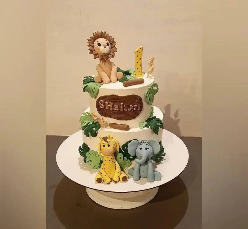 کیک تولد دو طبقه تم جنگل و سافاری برای تولد یک سالگی پسرانه با فیگور شیر، زرافه، فیل، عدد ۱ و اسم شاهان، از گروه تشریفاتی lemon.
