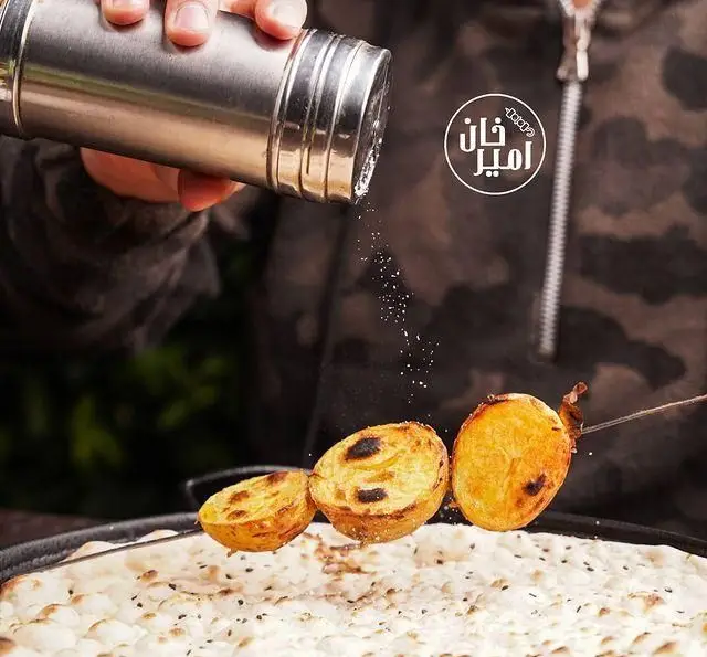 پاشیدن چاشنی روی سیب زمینی کبابی و نان داغ در جگرسرای امیرخان (گل یخ)، تجربه‌ای لذت‌بخش از طعم اصیل کباب.