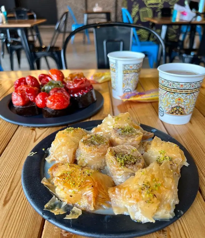 تصویری از باقلوای اصیل با پسته و شیره، دسرهای شکلاتی میوه‌ای و نوشیدنی‌های گرم در جگرسرای امیرخان (گل یخ). شیرینی سنتی و مدرن.