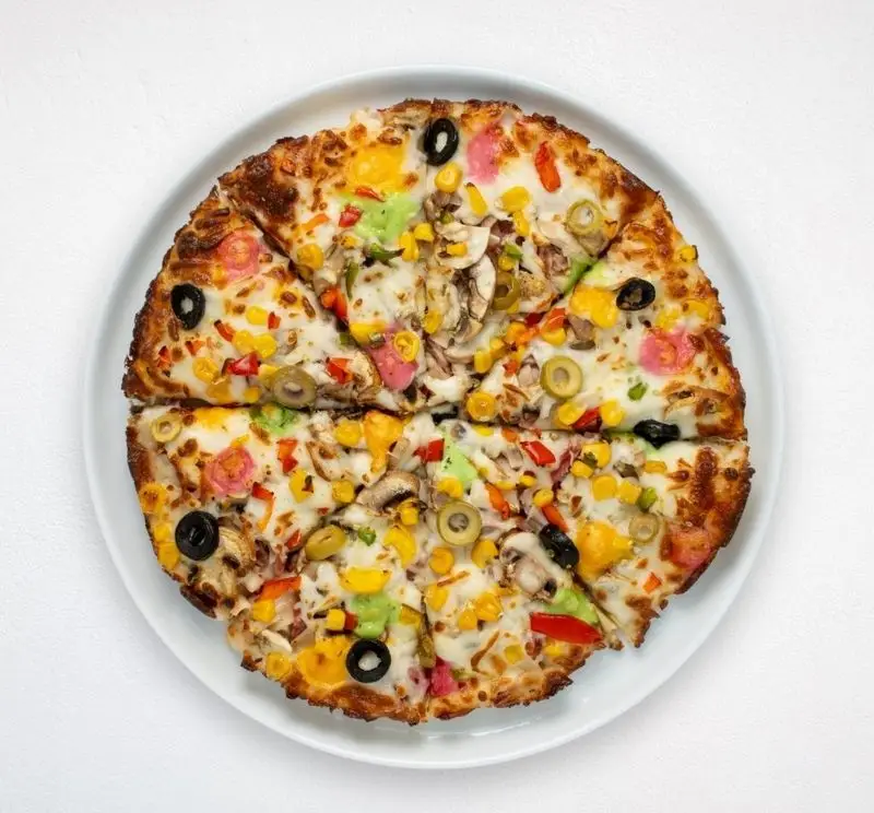 پیتزا رنگارنگ سبزیجات متنوع شامل ذرت، قارچ و زیتون، سرو شده روی سینی سفید از هایپر کترینگ چامه، بهترین فست فود ایرانی فرنگی.
