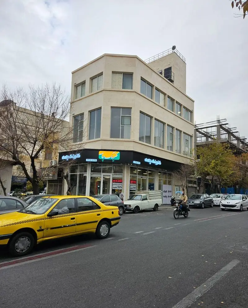 نمای بیرونی هایپر کترینگ چامه در خیابان، با تابلوی روشن و خودروهای مختلف از جمله تاکسی زرد. کترینگ غذای ایرانی، فرنگی و فست فود.