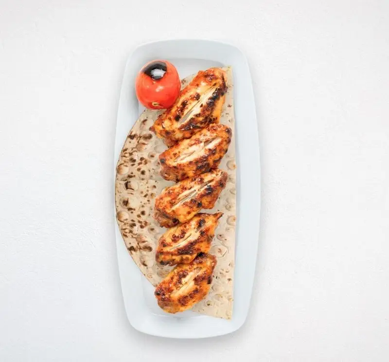 بال کبابی خوشمزه هایپر کترینگ چامه، غذای اصیل ایرانی. جوجه کباب بال با نان تازه و گوجه کبابی روی بشقاب سفید.