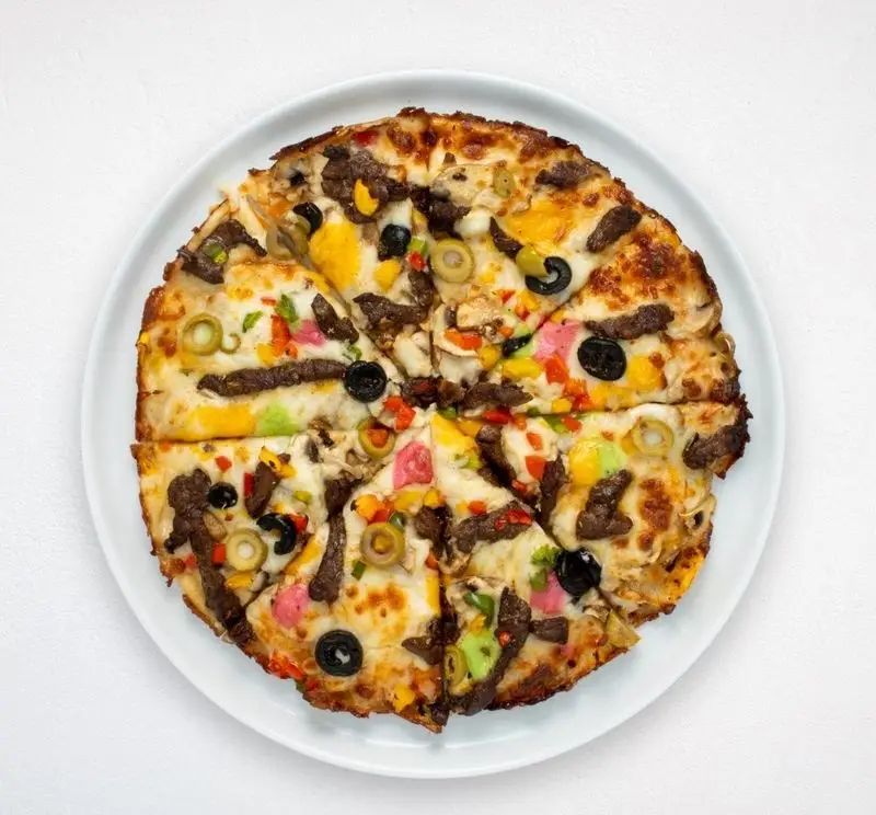 پیتزا گرد و اشتهاآور هایپر کترینگ چامه با برش‌های گوشت، زیتون سیاه و سبز، قارچ و فلفل دلمه‌ای رنگارنگ، سرو شده بر روی بشقاب سفید.