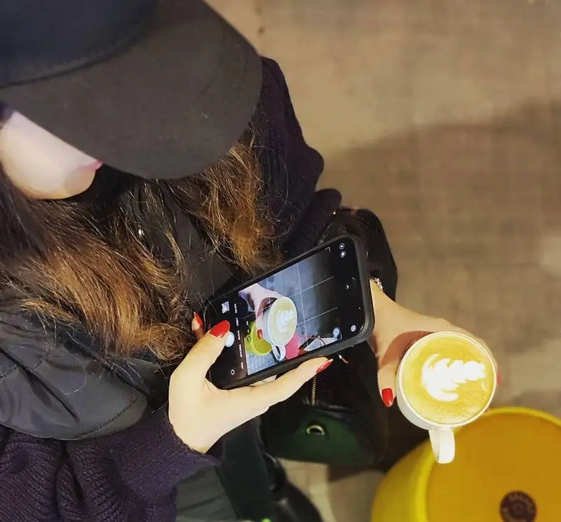 مشتری در کافه سامیا در حال عکس گرفتن از لاته آرت زیبای قهوه خود با موبایل است. تجربه دلنشین قهوه و عکاسی در کافه.