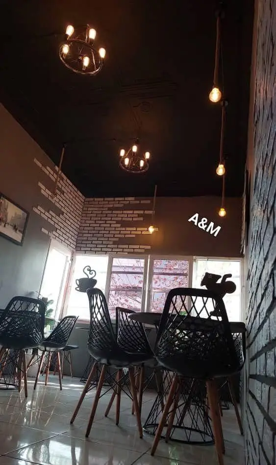 کافه قلیان عربی A&M: فضای داخلی شیک با سقف مشکی، لوسترهای چرخ‌دوچرخه‌ای، دیوارهای آجری، صندلی‌های مدرن و نماد قلیان.