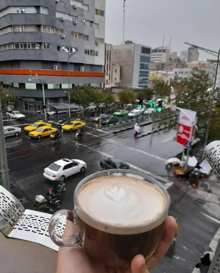 یک فنجان لاته گرم با طرح قلب بر فراز خیابان پرتردد و بارانی شهر، پیشنهاد کافه قلیان عربی A&M برای روزهای سرد.