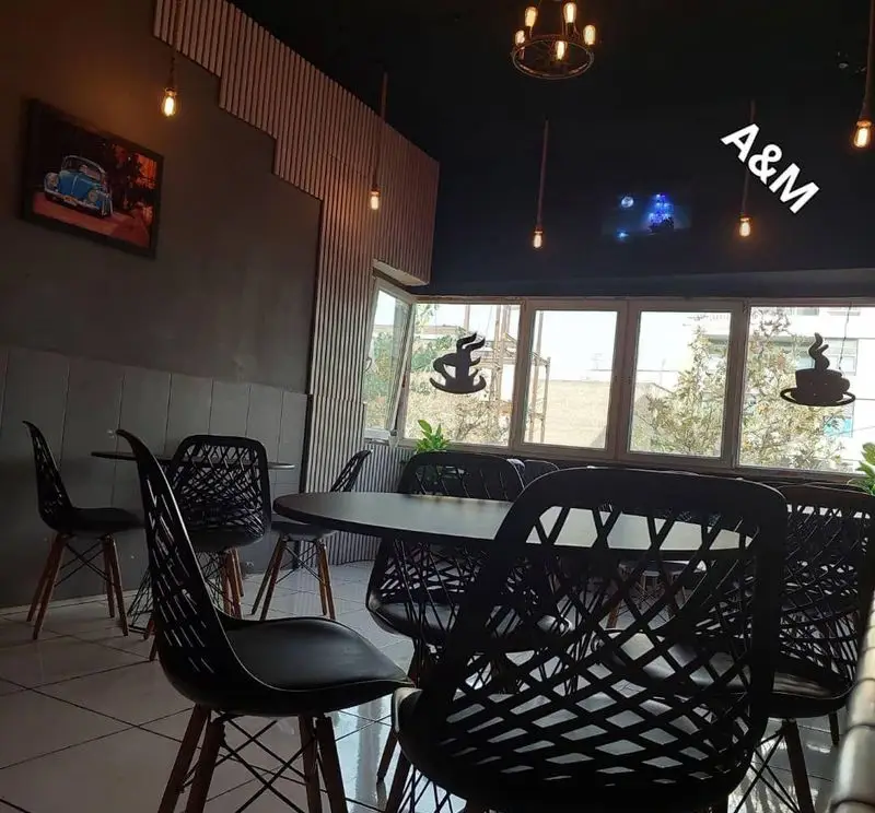 فضای داخلی کافه قلیان عربی A&M: چیدمان میز و صندلی مدرن، نورپردازی خاص، دیوارها با پنل چوبی و تابلوی ماشین کلاسیک، محیطی آرامش‌بخش