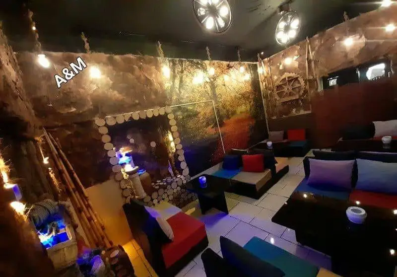 تصویری از کافه قلیان عربی A&M، فضایی دنج و سنتی با دکوراسیون طرح جنگل و چوب، مبلمان راحت و رنگی، نورپردازی گرم و جذاب، محیطی دلنشین برای مشتریان.