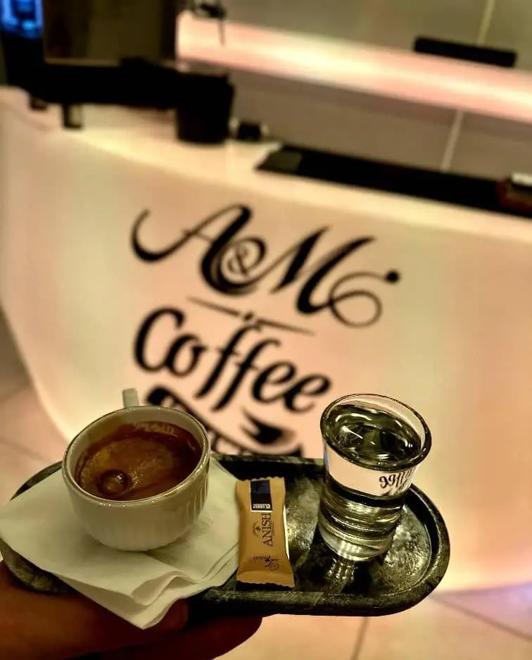 تصویری از یک فنجان قهوه اسپرسو با آب و شکر در سینی در کافه قلیان عربی A&M. لوگوی A&M Coffee بر روی میز پیشخوان.