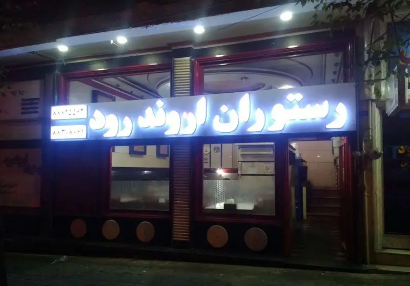 نمای شبانه و روشن رستوران اروند رود در تهران، با تابلوی نئون و شماره تلفن برای سفارش غذاهای ایرانی.