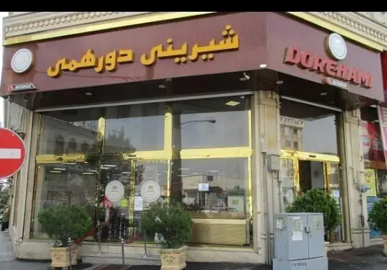 نمای بیرونی شیرینی فروشی دورهمی با تابلوی قهوه‌ای و نام Doreham، حروف برجسته طلایی، ویترین‌های شیشه‌ای بزرگ و دکوراسیون لوکس.