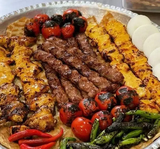 نمایی اشتهاآور از میز کباب‌های متنوع و لذیذ (جوجه و کوبیده) به همراه گوجه کبابی و پیاز در کافه رستوران شهرزاد.