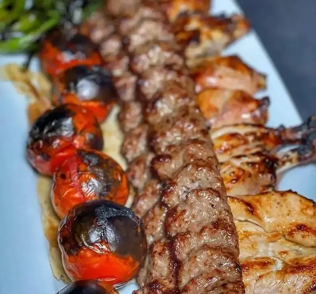 تصویر یک سینی لذیذ از کباب کوبیده و جوجه کباب کبابی، همراه با گوجه‌فرنگی‌های کبابی و فلفل سبز در کافه رستوران شهرزاد.