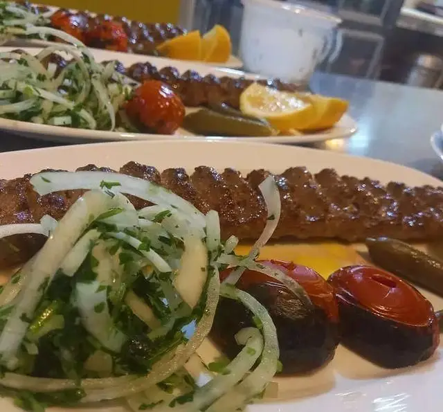 کباب کوبیده اصیل ایرانی کافه رستوران شهرزاد با گوجه کبابی، پیاز، جعفری و لیمو. لذت غذای سنتی و خوشمزه در فضایی دلنشین.