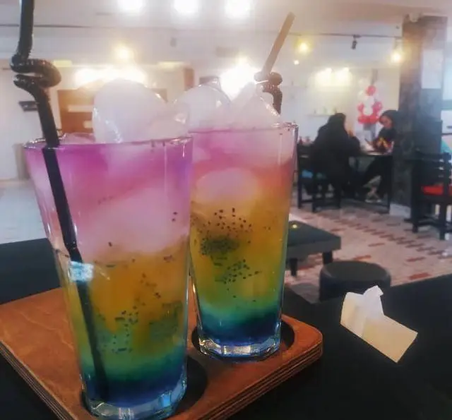 دو نوشیدنی رنگارنگ و خنک با لایه‌های جذاب و تخم شربتی در کافه رستوران شهرزاد، تجربه‌ای دلپذیر در محیطی آرام و مدرن.