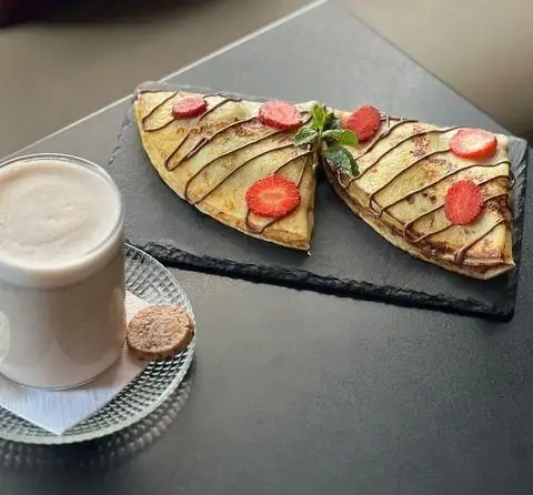 کرپ‌های خوشمزه کافه اوان با سس شکلات، توت فرنگی تازه و نوشیدنی دلپذیر، ایده‌آل برای صبحانه یا عصرانه‌ای شیرین.