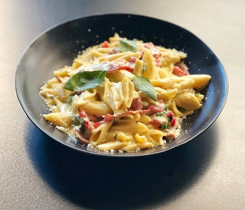 پاستا پنه خامه ای لذیذ با سس آلفردو، تکه های ژامبون، پنیر پارمزان و برگ ریحان تازه، آماده سرو در کافه اوان.