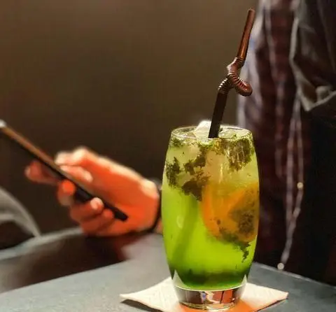 نوشیدنی خنک و دلپذیر در کافه اوان با برگ نعنا، لیمو و یخ. لذت اوقات فراغت و استفاده از گوشی موبایل در فضای دنج کافه.