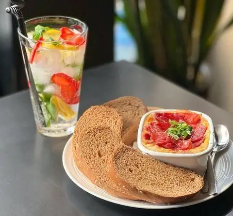 یک نوشیدنی خنک با توت فرنگی، لیمو و نعنا در کنار صبحانه یا عصرانه ویژه کافه اوان شامل نان کامل و خوراک لذیذ.