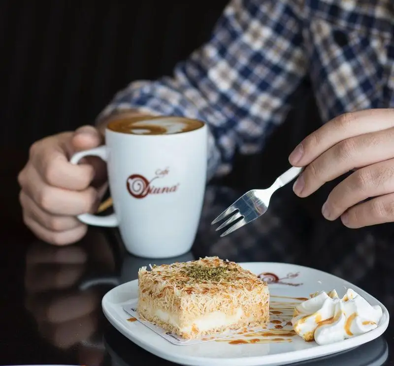 لذت‌بردن از قهوه کاپوچینو با لاته آرت و دسر کرم‌دار و شیرین کافه ویونا، تزئین شده با رشته‌های کادایف، پودر پسته، خامه و سس کارامل.