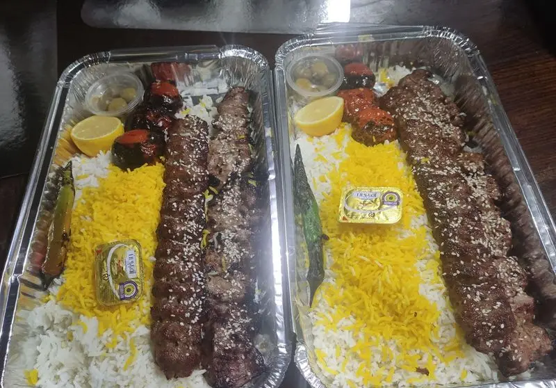 دو سینی کباب کوبیده تهیه غذای تایماز با برنج سفید و زعفرانی، گوجه کبابی، لیمو، زیتون و کره در ظرف‌های آلومینیومی.