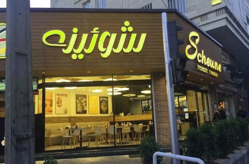 تصویر نمای خارجی فست فود شورینه با تابلوی نئونی درخشان سبز-زرد، طراحی مدرن و جزئیات چوبی. فضای داخلی روشن و دلپذیر رستوران.