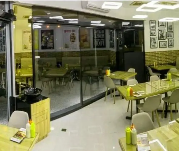 نمایی از فضای داخلی دنج و مدرن فست فود شورینه با میزهای چوبی روشن، صندلی‌های راحت و دکوراسیون آجری شیک.