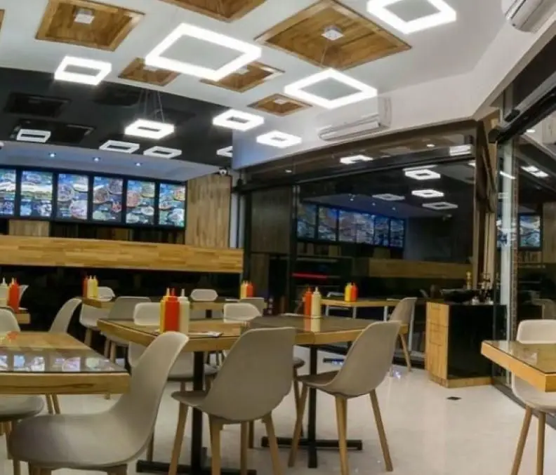 دکوراسیون داخلی فست فود شورینه، محیطی مدرن و روشن با میزهای چوبی، صندلی‌های شیک و نمایشگرهای منوی دیجیتال رنگارنگ.