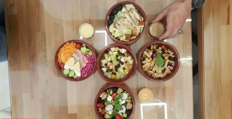 چیدمان زیبای انواع سالادهای تازه و خوشمزه فست فود شورینه، شامل سزار، میوه، پاستا و گزینه‌های متنوع دیگر برای وعده‌های سالم و دلچسب.