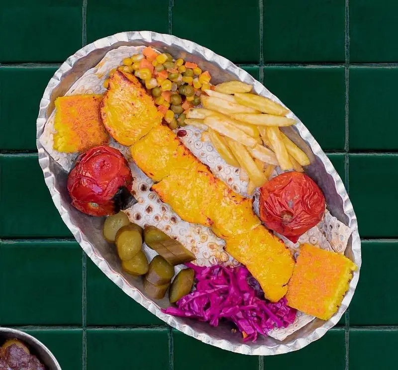 یک سینی رنگارنگ از جوجه کباب زعفرانی رستوران سدره، همراه با ته چین، گوجه کبابی، سیب‌زمینی و مخلفات تازه. مناسب برای ناهار و شام.