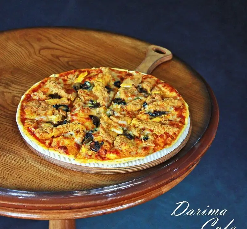 پیتزای گوشت و زیتون کافه رستوران داریما، با پنیر فراوان و نان ترد، روی تخته سرو چوبی برای مشتریان گرامی.