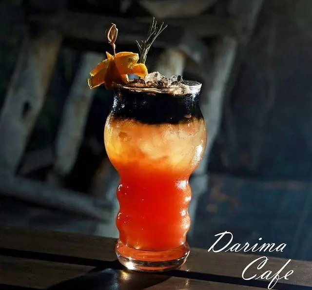 کوکتل لایه‌ای و جذاب کافه رستوران داریما، با ترکیب رنگ‌های منحصر به فرد، تزئین شده با پرتقال و رزماری برای طعمی خاص.