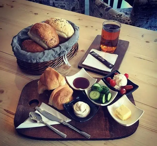 صبحانه کامل کافه رستوران داریما: نان، کروسان، چای، مربا، پنیر، کره، خیار و گوجه گیلاسی سرو شده روی تخته چوبی.