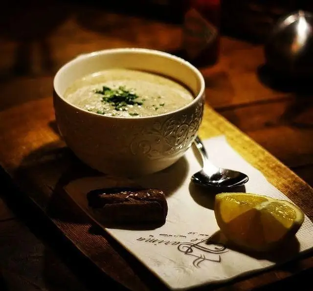 نمایی دلنشین از یک کاسه سوپ گرم و خوش‌طعم، تزئین شده با سبزیجات، سرو شده در کافه رستوران داریما. همراه با نان و لیمو، روی تخته چوبی، تجربه‌ای خاص از منوی ما.