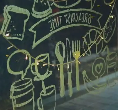 تصویر طرح "BREAKFAST TIME" (معکوس) با نقاشی گچی جذاب صبحانه، نان تست، قهوه و دونات در پنجره کافه رستوران داریما.