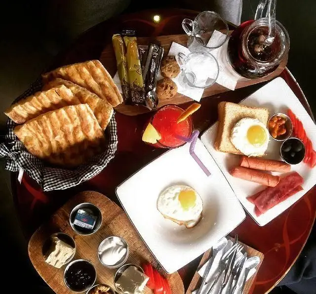 میز صبحانه مفصل و متنوع کافه رستوران داریما با تخم مرغ، نان تازه، سوسیس، بیکن، زیتون، مربا و نوشیدنی.