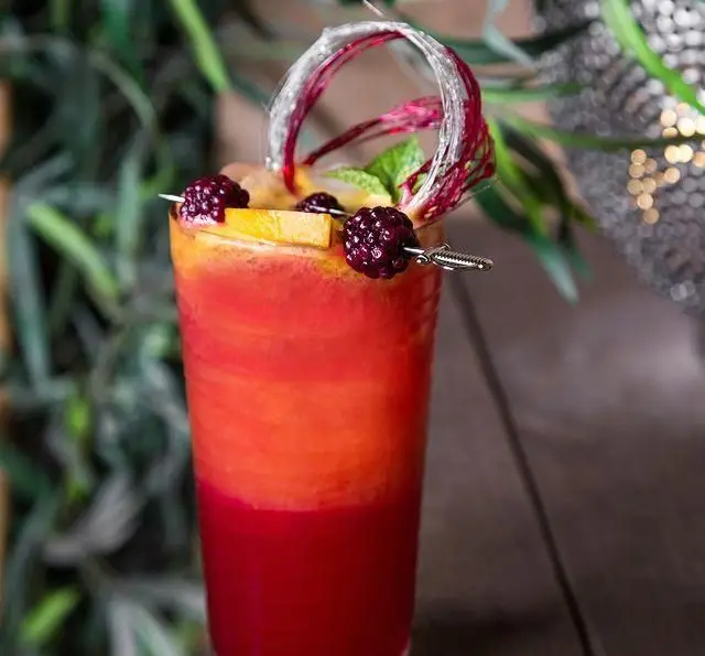 نوشیدنی لایه ای میوه ای تازه و رنگارنگ در کافه رستوران عربی مدائن، با تزیین شاه توت، پرتقال و نعناع.